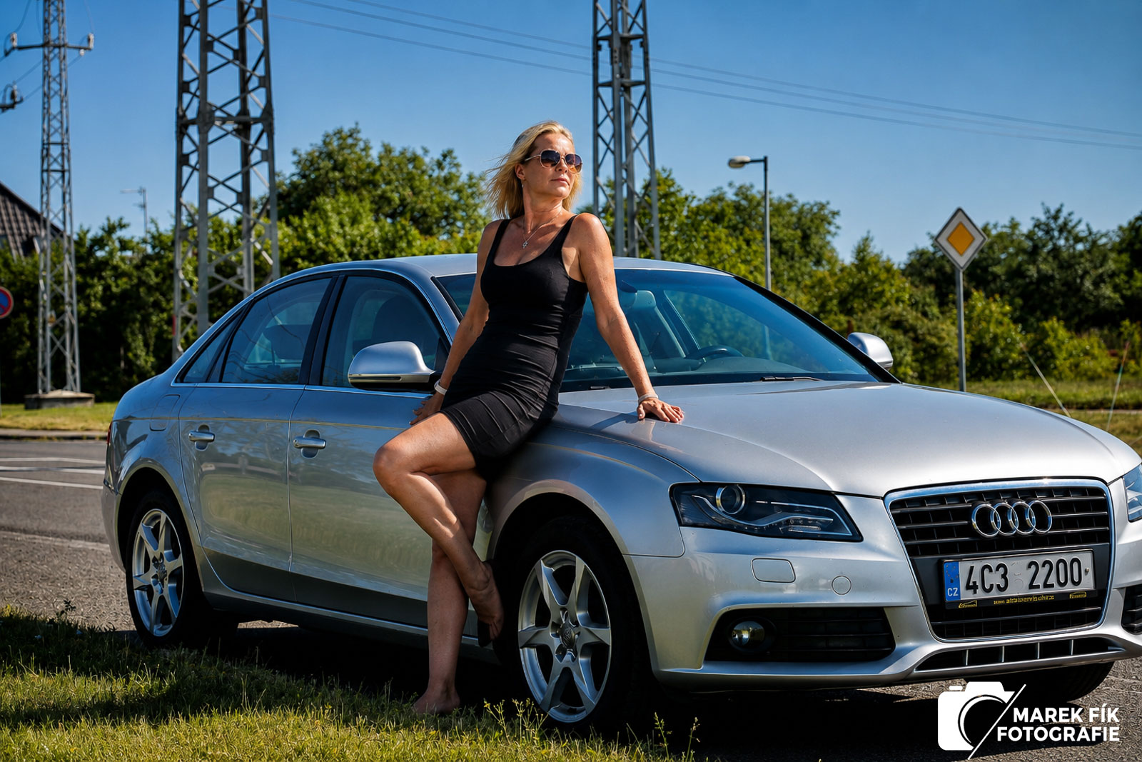 Portrét ženy sedící na kapotě stříbrného Audi